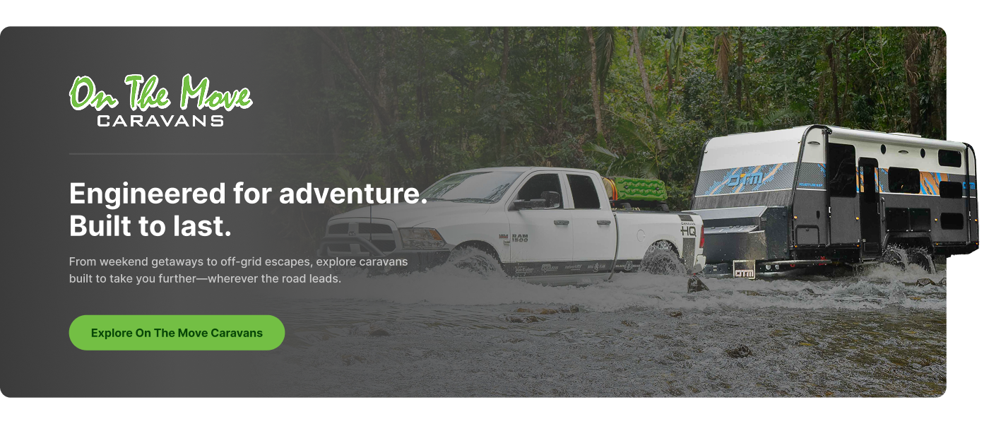 A white off-road truck towing a rugged camper trailer across a shallow river surrounded by dense forest.