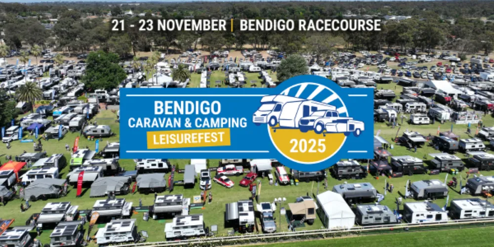 Aerial view of the Bendigo Caravan & Camping Leisurefest showing rows of caravans, camper trailers, and exhibitor tents set up on grassy grounds beside a racetrack, with trees and buildings in the background.