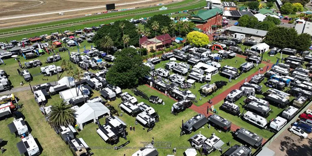 Aerial view of the Bendigo Caravan & Camping Leisurefest showing rows of caravans, camper trailers, and exhibitor tents set up on grassy grounds beside a racetrack, with trees and buildings in the background.